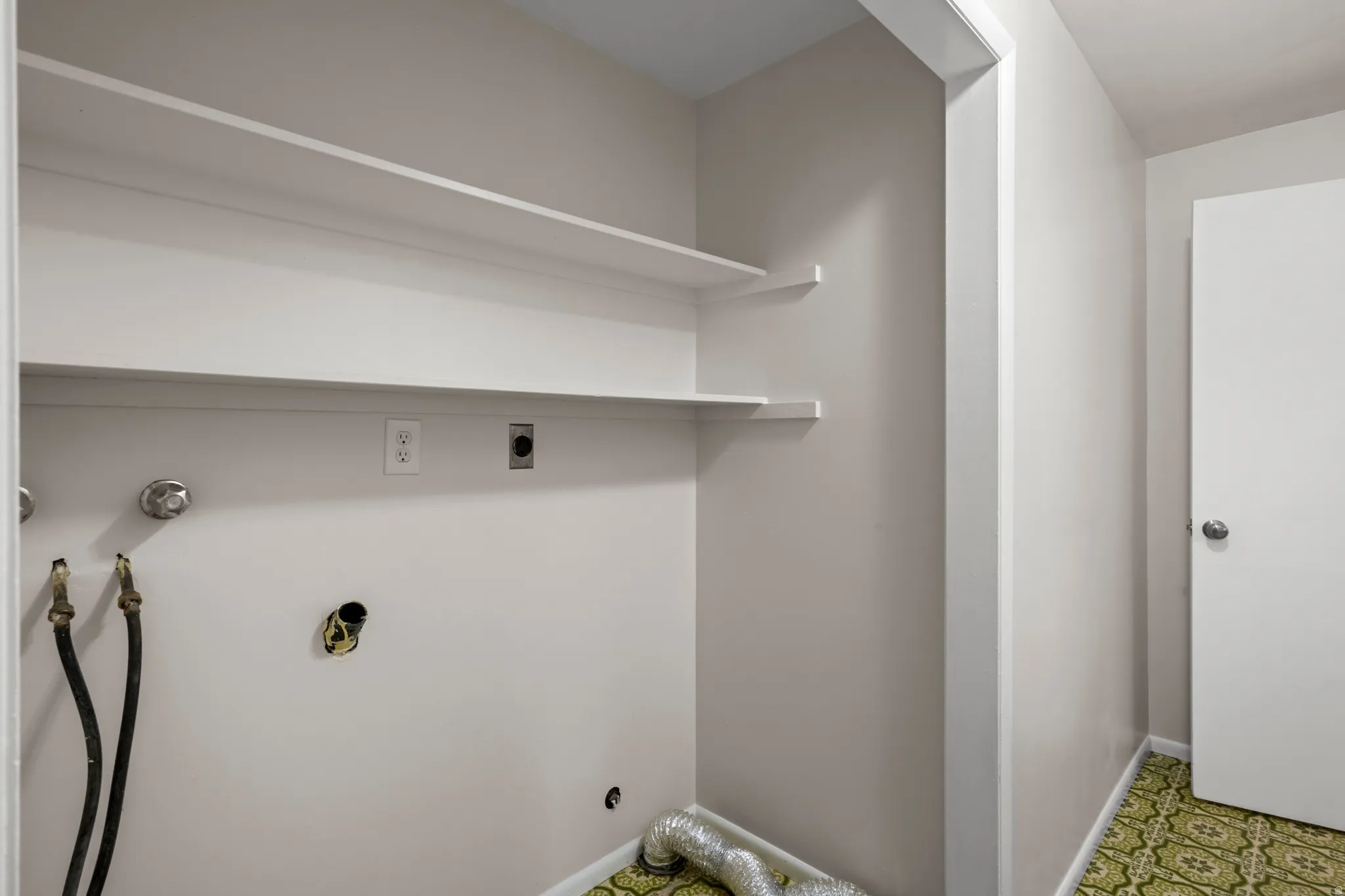 Laundry area featuring dual wall-mounted shelving, appliance hookups, and patterned green flooring