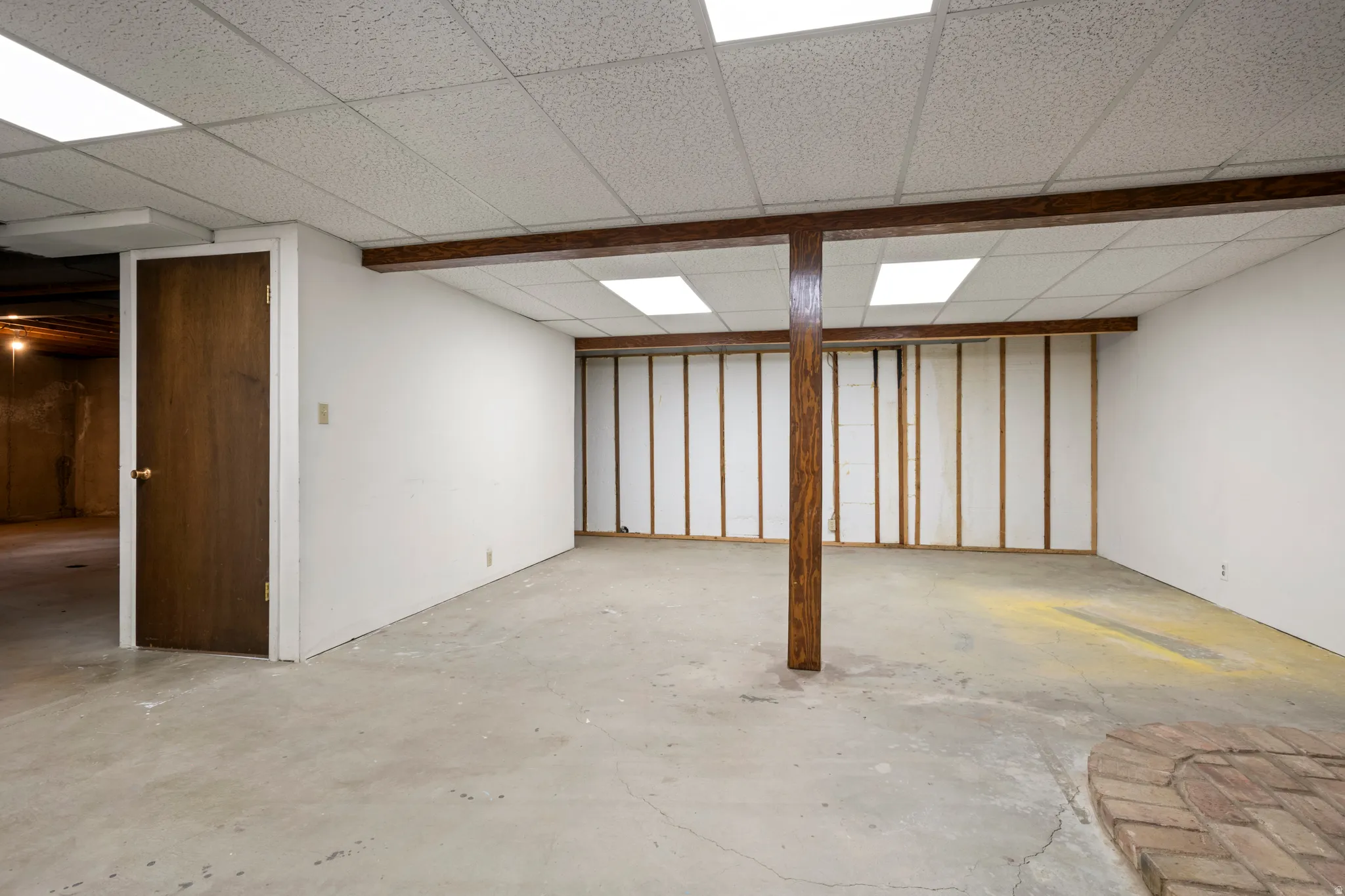 Spacious lower level featuring a drop ceiling with integrated lighting, exposed wood support beams, and a concrete floor