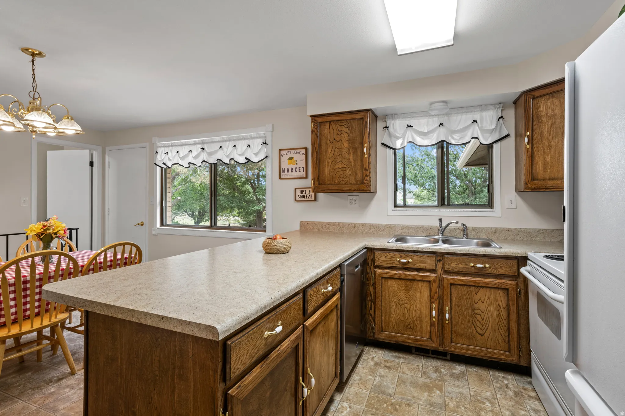 Kitchen featuring wood-finish cabinetry, a double basin stainless steel sink, and light-toned countertops