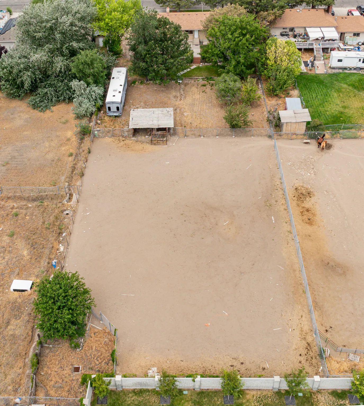 Expansive outdoor area featuring a large cleared earth pad, perimeter fencing, mature trees, and a detached shed structure