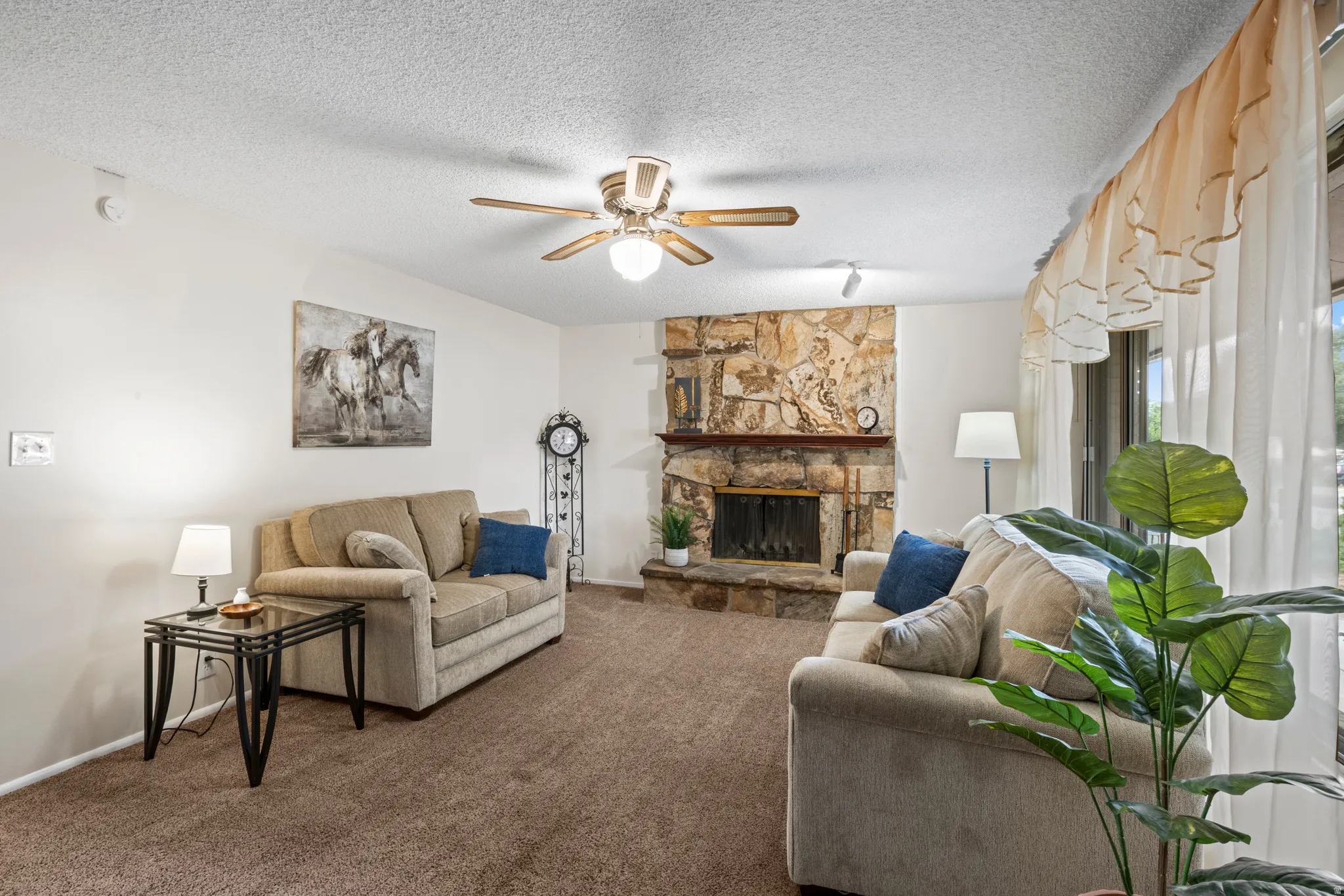 Living area featuring a stone-clad fireplace, ceiling fan, carpeted flooring, and sliding glass door