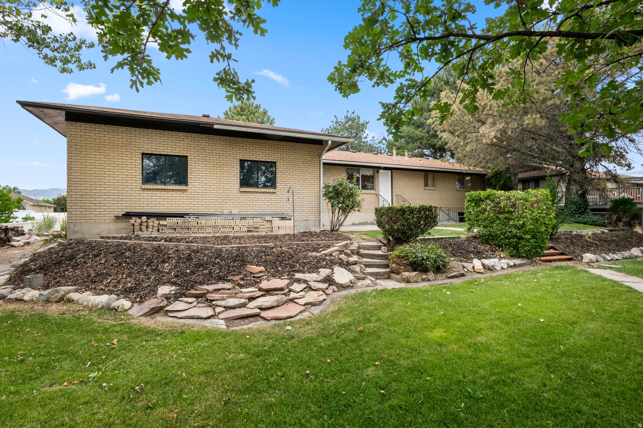 Manicured lawn with mature trees, and tiered landscaping featuring decorative rock and mulch beds