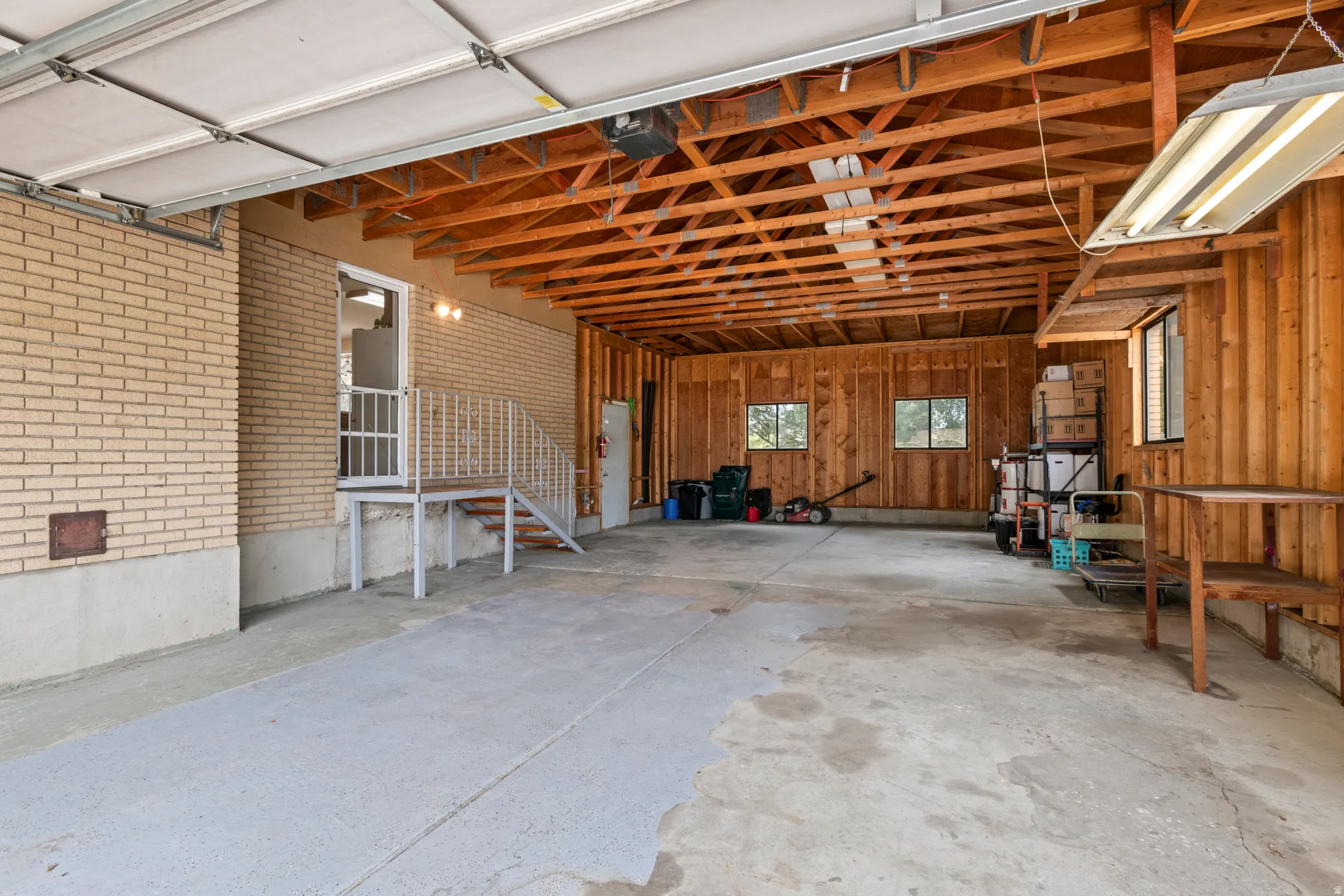 Spacious garage featuring a light brick wall, exposed wood beam ceiling, concrete flooring, and windows providing natural light