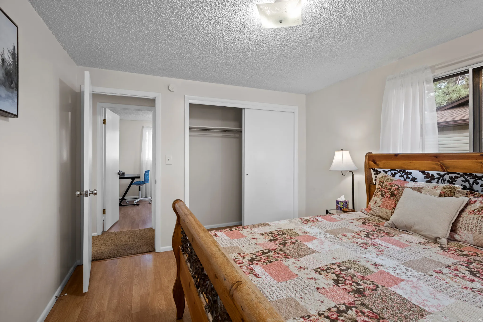 Bedroom featuring wood-finish flooring, a double-door closet, and a window with white sheer curtains