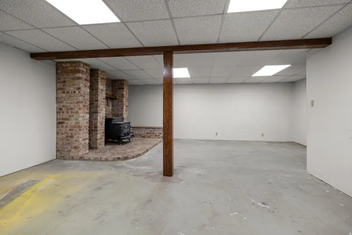Spacious room featuring a brick-clad wood-burning stove with a matching brick hearth, exposed wood beam, and suspended acoustic tile ceiling