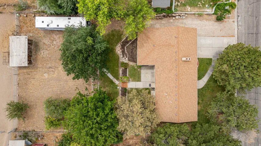 Expansive lot featuring a single-story residence with a brown shingle roof, concrete driveway, and mature landscaping