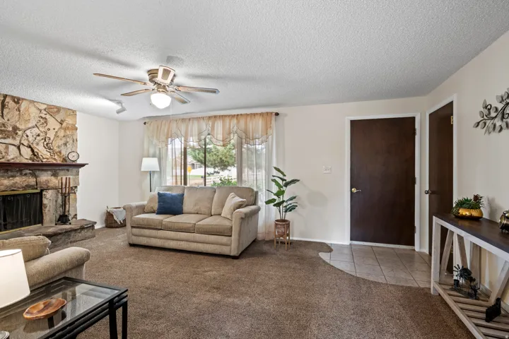 Living area featuring a stone fireplace with a raised hearth, broad window with sheer treatments, and a ceiling fan