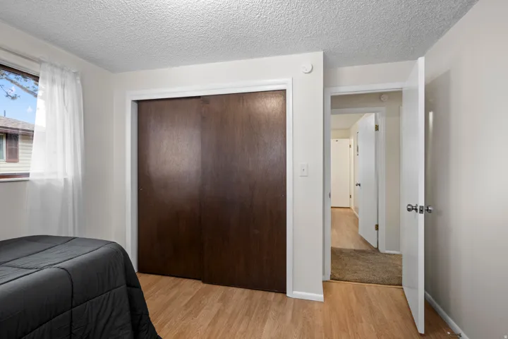 Wood-finish flooring throughout, featuring a window with white trim, a built-in closet with dark wood-finish sliding doors, and a white interior door