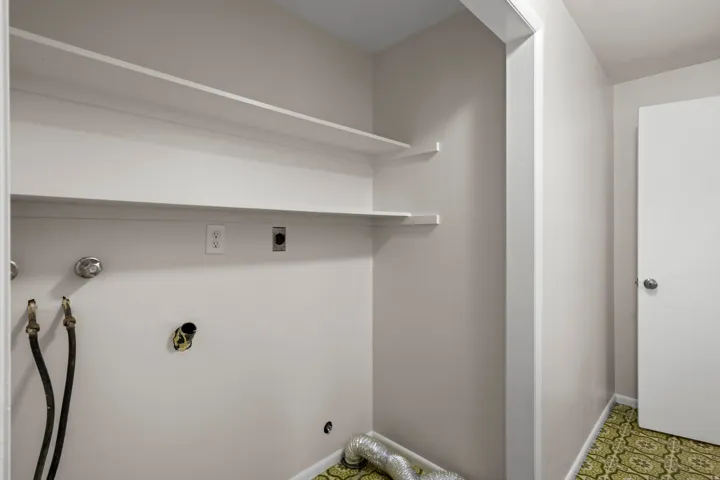Laundry area featuring dual wall-mounted shelving, appliance hookups, and patterned green flooring