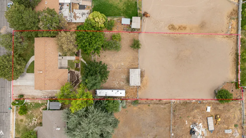 Expansive lot featuring a single-story residence with a brown shingle roof, mature perimeter trees, a concrete driveway.