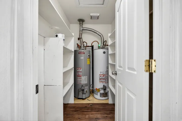 Utility closet featuring two water heaters, built-in shelving, and wood-finish flooring