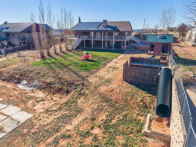 Spacious backyard featuring a sloped grassy area, mature deciduous trees, and a multi-level play structure with a fenced enclosure