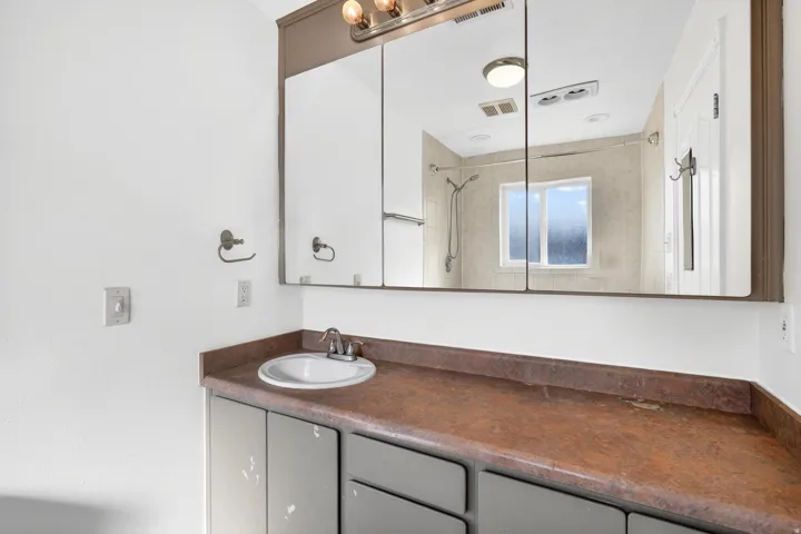 Bathroom vanity featuring a single basin sink, laminate countertop, and built-in medicine cabinet with integrated lighting