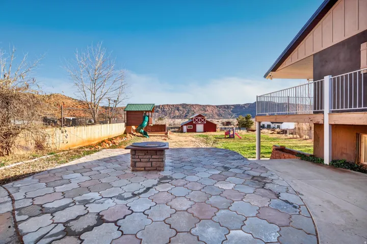 Expansive paver patio featuring a stone fire pit, bordered by a concrete walkway