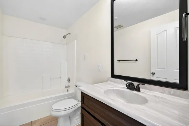 Bathroom featuring a tub/shower combination with white subway tile surround, a dark wood-finish vanity, a white countertop with an integrated sink, and bronze-finish fixtures