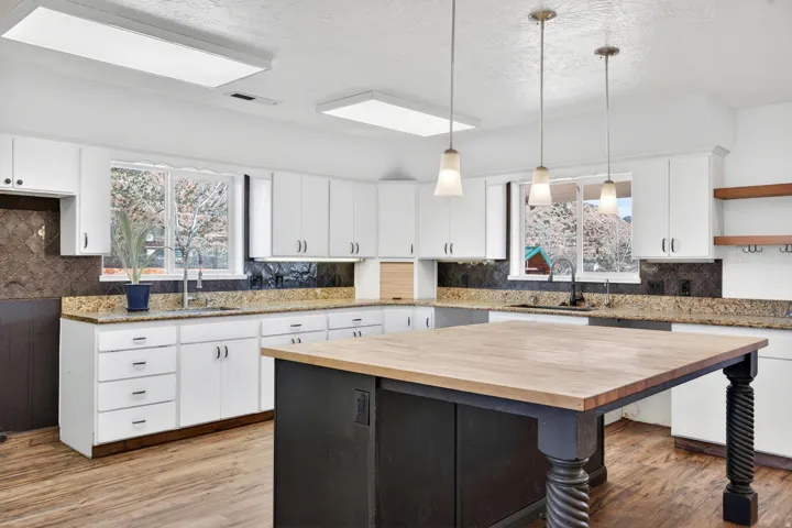 Kitchen featuring a central island with a wood-finish countertop and dark base, white cabinetry, granite countertops, and wood-finish flooring