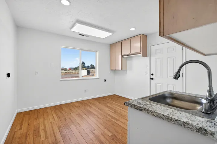 Utility area featuring wood-finish flooring, a stainless steel sink with a gooseneck faucet, light-toned cabinetry, and a window providing natural illumination