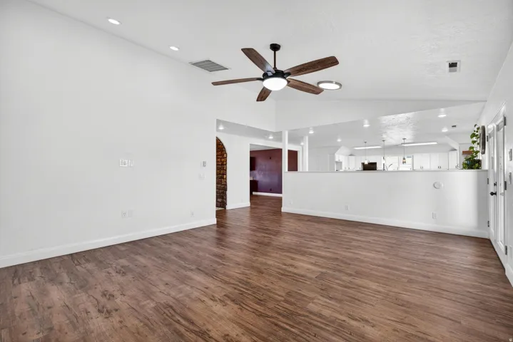 Spacious living area featuring wood-finish flooring, a ceiling fan with light, recessed lighting, and a half-wall partition