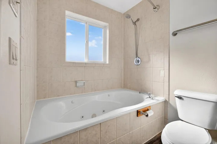 Built-in jetted tub with tiled surround, adjacent window, and wall-mounted shower fixture