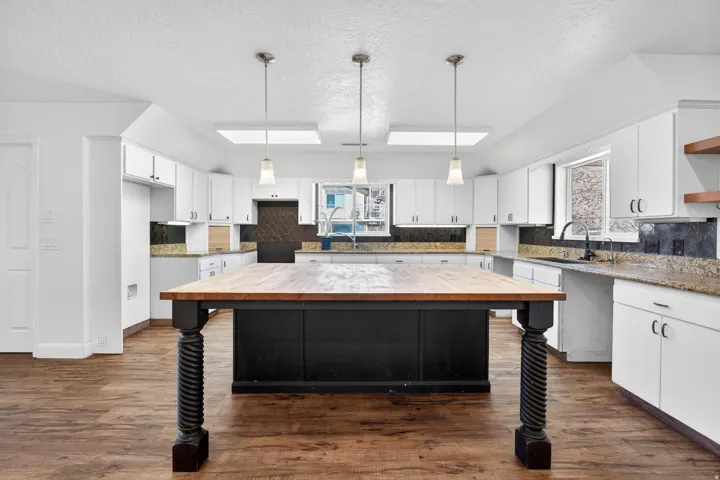 Spacious kitchen featuring an expansive wood-top island with turned legs, wood-finish flooring, white cabinetry, granite countertops, and pendant lighting