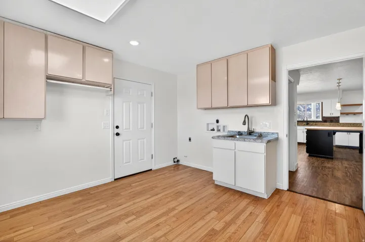 Utility area with wood-finish flooring, white walls, and light-colored cabinetry