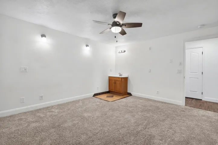 Spacious room featuring neutral carpeting, a ceiling fan with integrated lighting, and two wall sconces