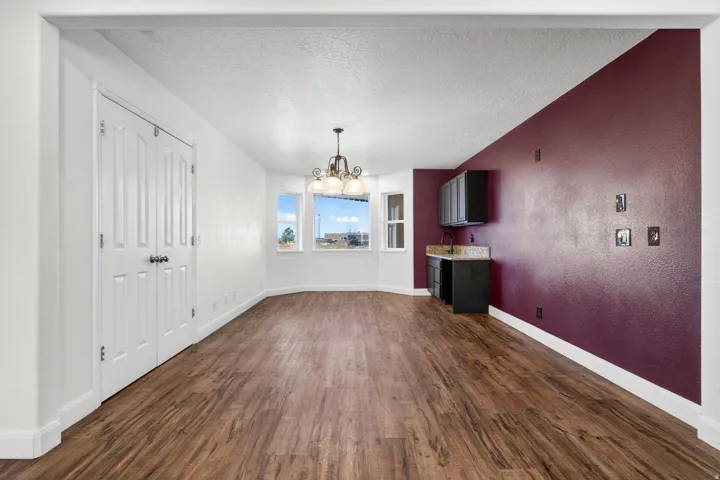 Spacious room featuring wood-finish flooring, a built-in wet bar with dark cabinetry and a stone-look countertop, multiple windows, and a chandelier lighting fixture