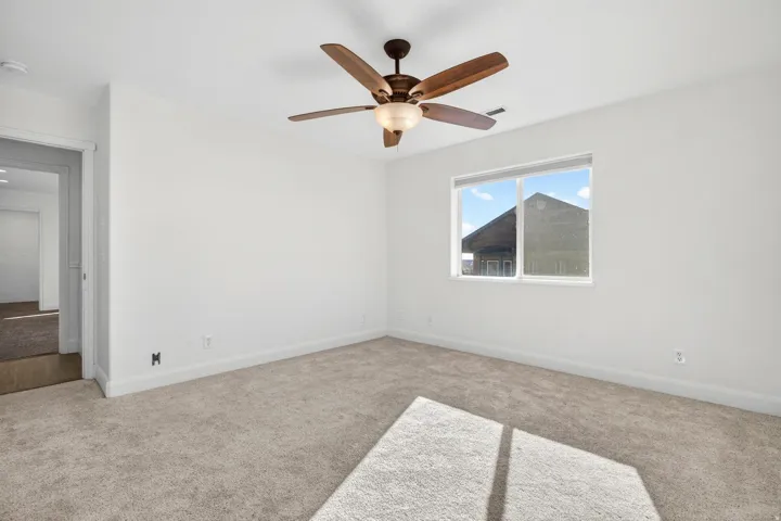 Bright interior space featuring a double-paned window, neutral carpet, white baseboards, and a wood-finish ceiling fan with integrated lighting