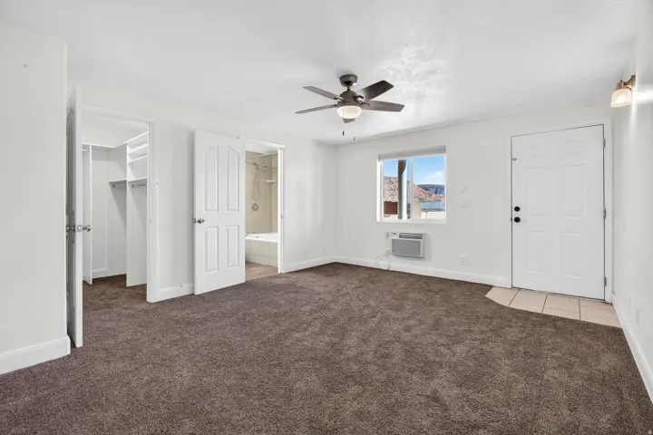 Spacious room featuring plush carpet flooring, a window offering distant mountain scenery, and a ceiling fan with integrated lighting