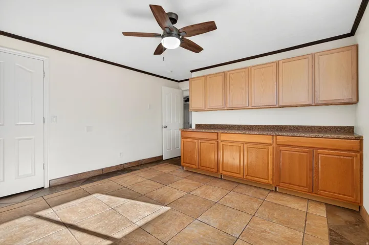 Room featuring extensive cabinetry with a stone-finish countertop, ceiling fan with light fixture, and tile flooring