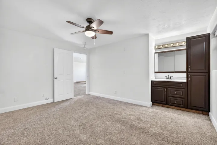 Carpeted room featuring a ceiling fan with integrated lighting, a white painted door, and a built-in vanity area