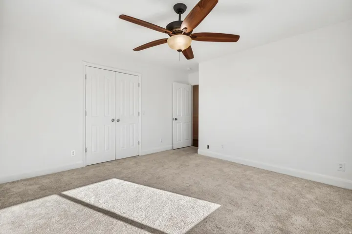 Carpeted room featuring a ceiling fan with light fixture, white walls, and bi-fold closet doors