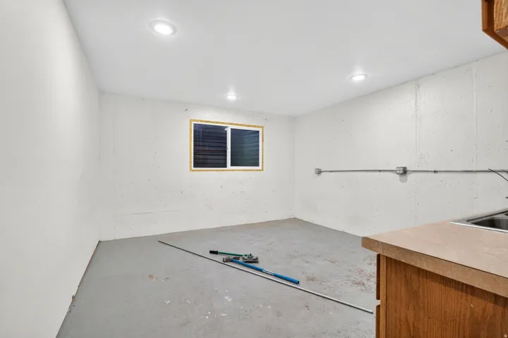 Unfinished basement space featuring a single window, recessed lighting, concrete walls, concrete flooring, and a built-in utility sink with wood-finish cabinetry