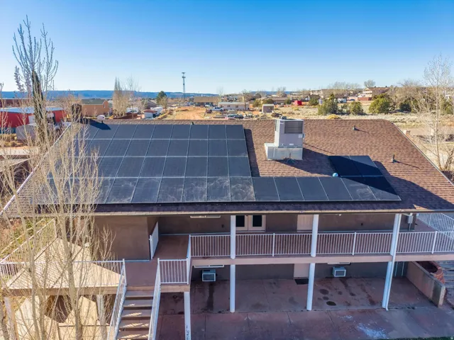 Rooftop solar panels on a brown shingle roof, complemented by a covered balcony with white railings