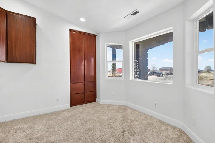 Recessed lighting illuminates a space featuring light-toned carpeting, white baseboards, and white walls
