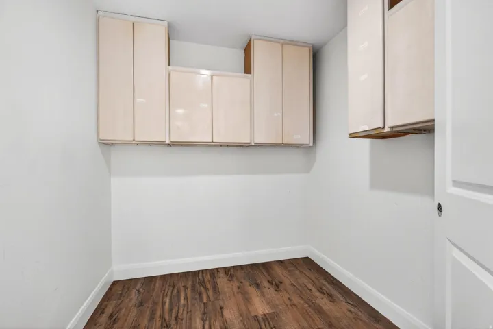 Utility space featuring wood-finish flooring, white walls, and built-in upper cabinetry