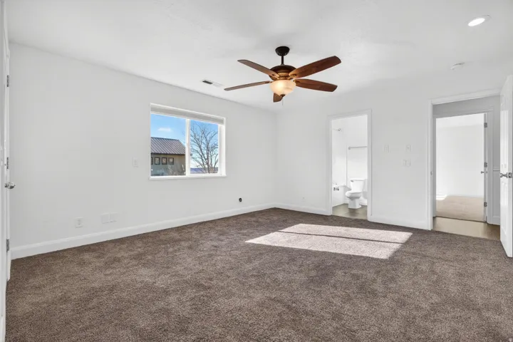 Spacious room featuring neutral carpeting, a ceiling fan with integrated lighting, and a white trim window