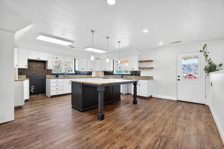Spacious kitchen featuring a dark wood-finish island, white cabinetry, recessed lighting, and wood-finish flooring