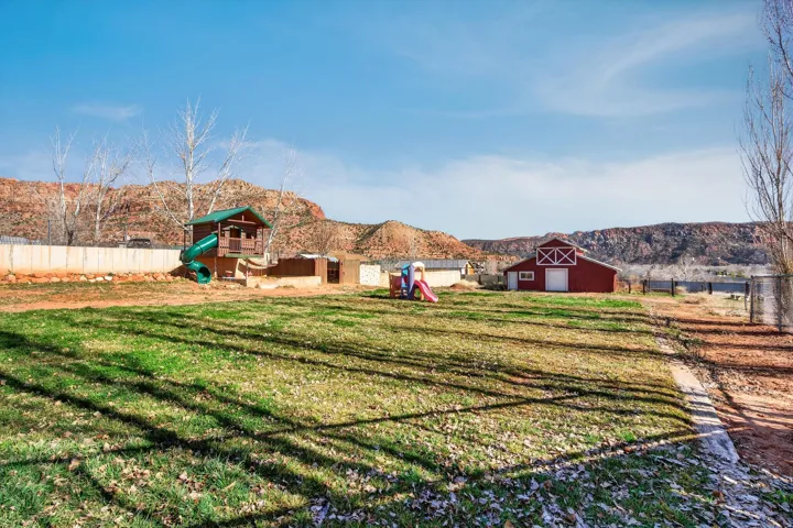 Expansive grounds featuring a red barn-style outbuilding, a perimeter fence, and distant natural rock formations