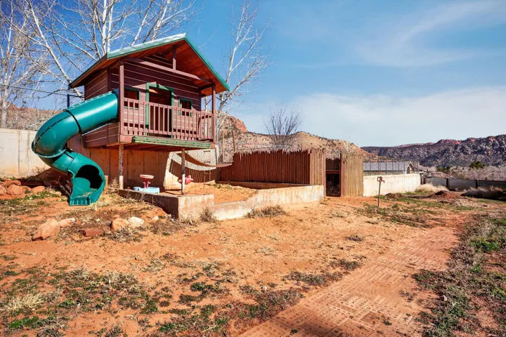 Elevated wooden playhouse with an attached green slide, set within a fenced outdoor area