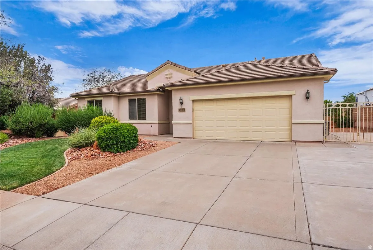Stucco exterior with a tiled roof, featuring an attached garage with a panel door, decorative exterior lighting, and a paved driveway