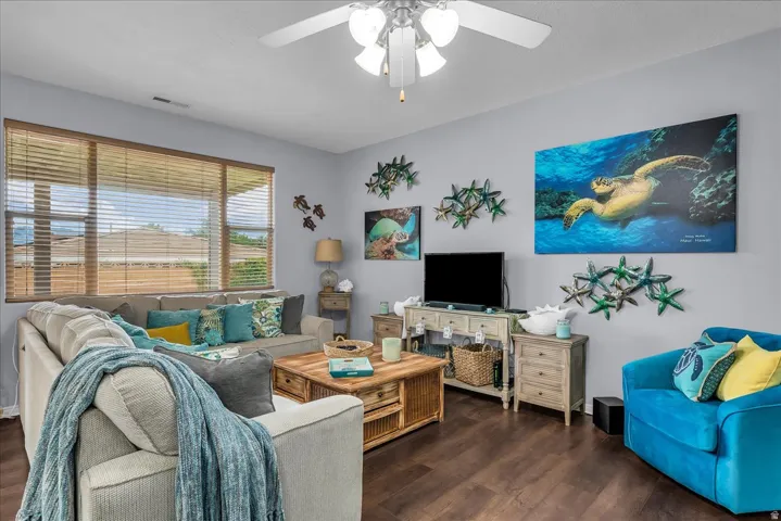 Living area featuring wood-finish flooring, a ceiling fan with integrated lighting, and multiple windows with horizontal blinds