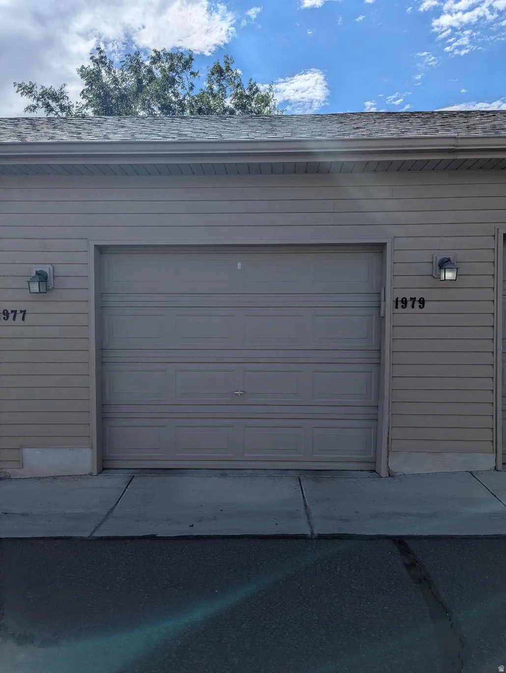 Attached garage with panel door, exterior wall sconces, and vinyl siding