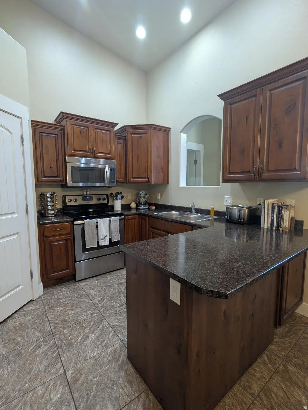 Kitchen featuring wood cabinetry, dark speckled countertops, stainless steel appliances, and tile flooring