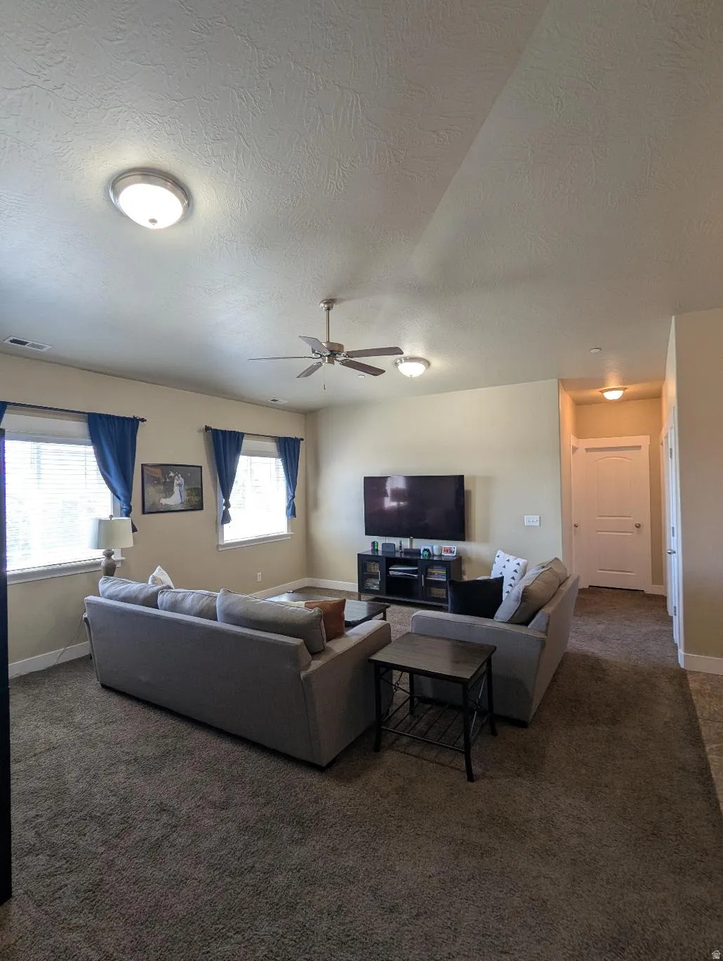 Spacious living area featuring neutral-toned walls and dark textured carpeting