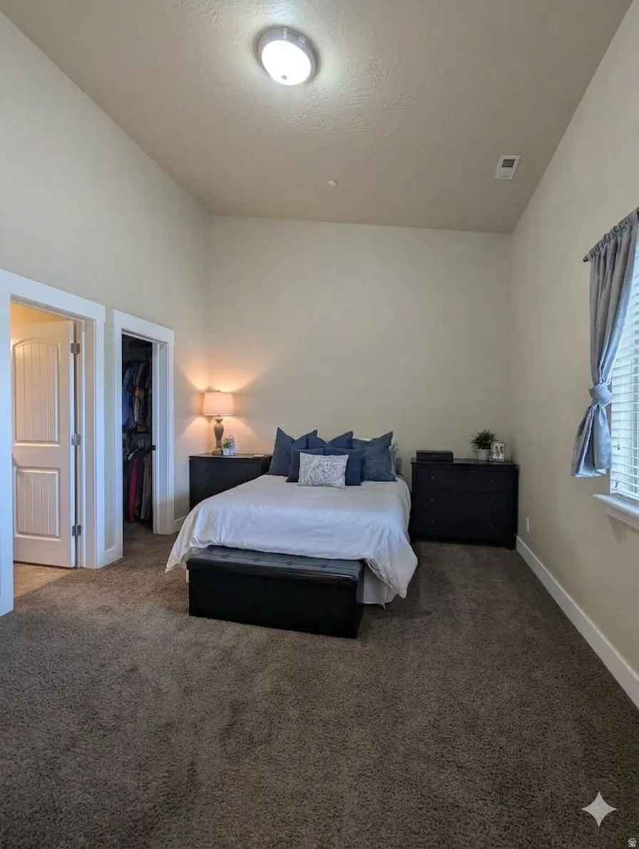 Neutral-toned carpeting extends throughout the room, complemented by a window with blinds and drapes