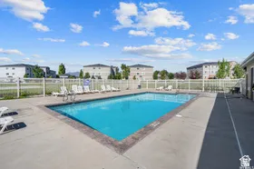 Rectangular outdoor swimming pool with a concrete surround, white perimeter fencing, and surrounding low-rise buildings