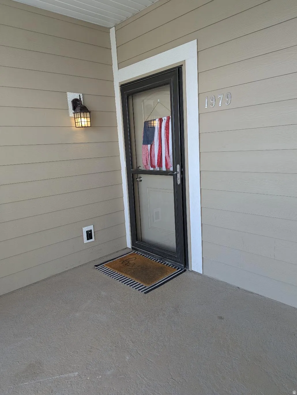 Entryway featuring tan siding, a black storm door, white trim, and a concrete patio
