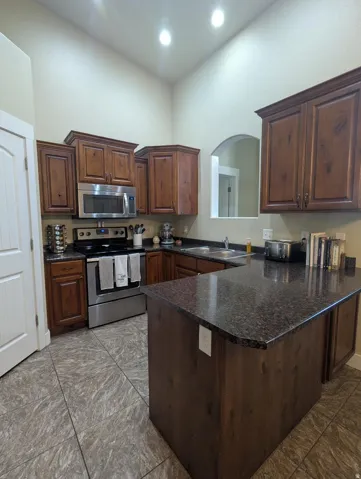 Kitchen featuring wood cabinetry, dark speckled countertops, stainless steel appliances, and tile flooring