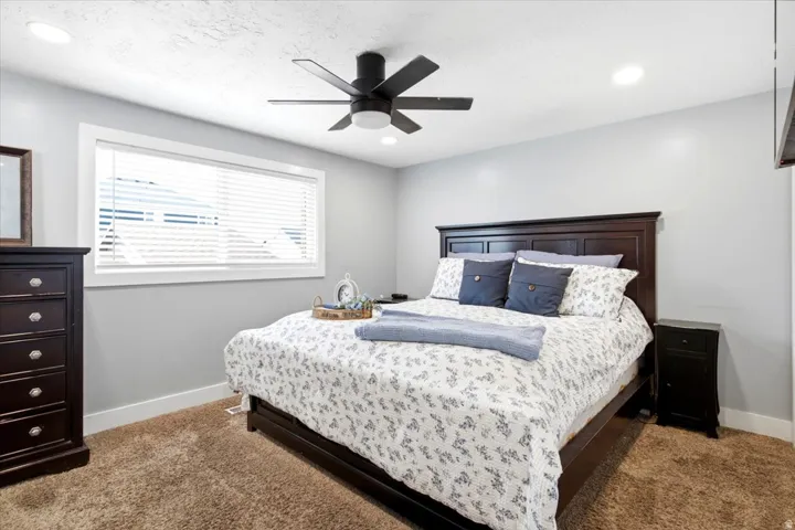 Bedroom featuring textured carpeting, a horizontal window with white blinds, and a ceiling fan with integrated lighting